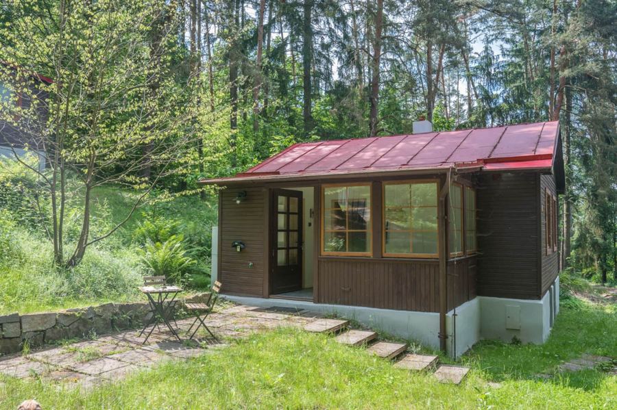 Dřevěná chata s prosklenou verandou mezi stromy
